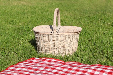 Photo of Picnic basket and checkered tablecloth on green grass outdoors