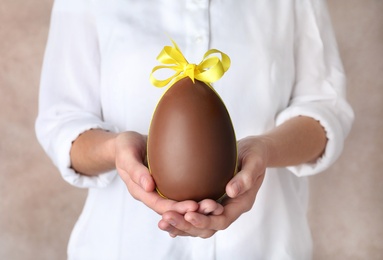 Photo of Woman holding chocolate Easter egg with bow knot on color background, closeup