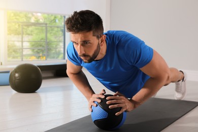 Athletic man doing push ups with medicine ball in modern gym