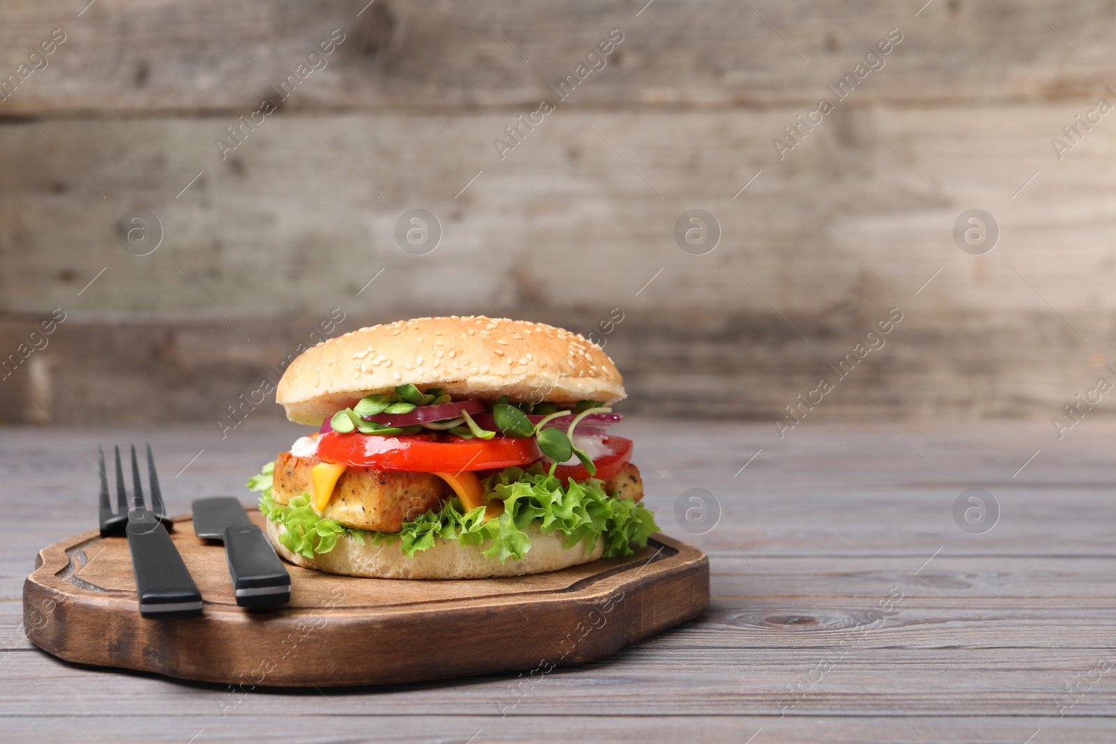 Photo of Delicious burger with tofu and fresh vegetables served on grey wooden table. Space for text