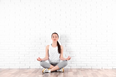 Young woman meditating on floor near brick wall, space for text. Zen concept