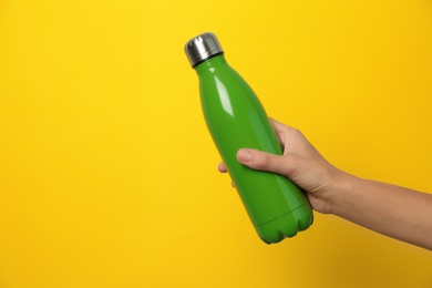 Woman holding modern green thermos on yellow background, closeup. Space for text