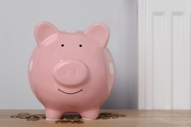 Piggy bank and coins on wooden table near heating radiator, space for text