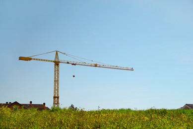 Modern construction crane near meadow on sunny spring day