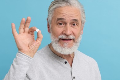 Senior man with pill on light blue background