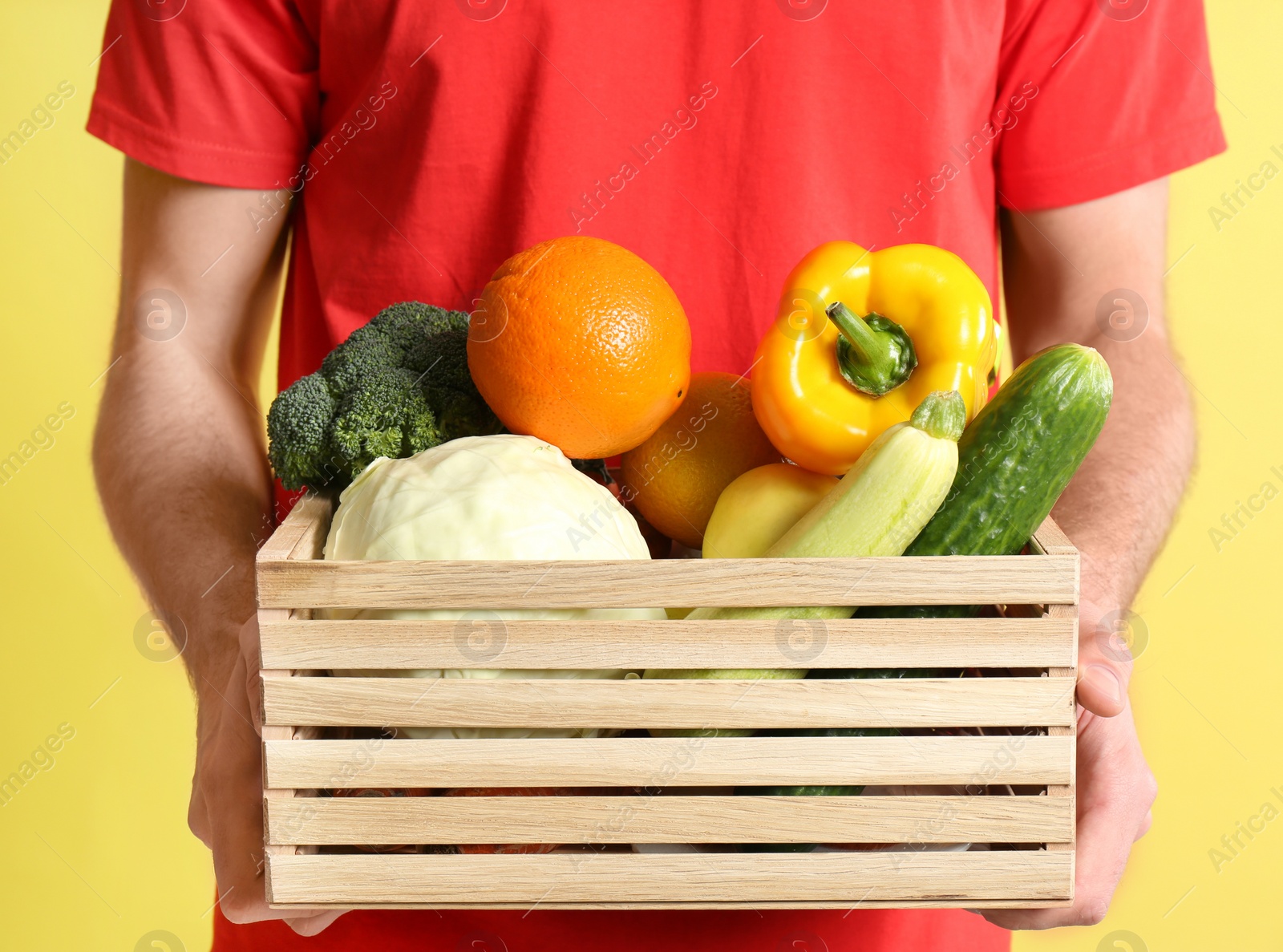 Photo of Courier with fresh products on yellow background, closeup. Food delivery service