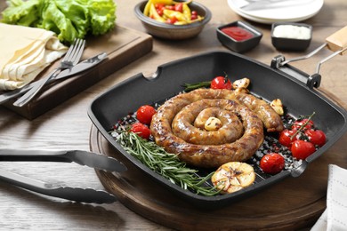 Photo of Delicious homemade sausage with garlic, tomatoes, rosemary and spices served on wooden table, closeup