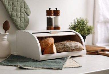 Wooden bread basket with freshly baked loaves on white marble table in kitchen