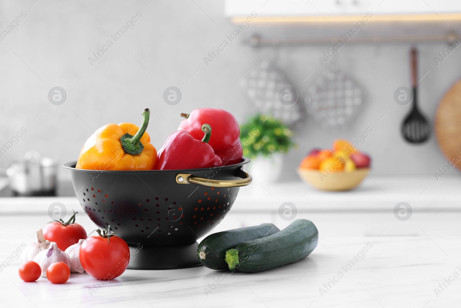 Photo of Black colander and different vegetables on white marble table in kitchen. Space for text