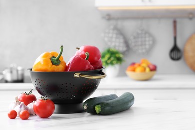 Black colander and different vegetables on white marble table in kitchen. Space for text