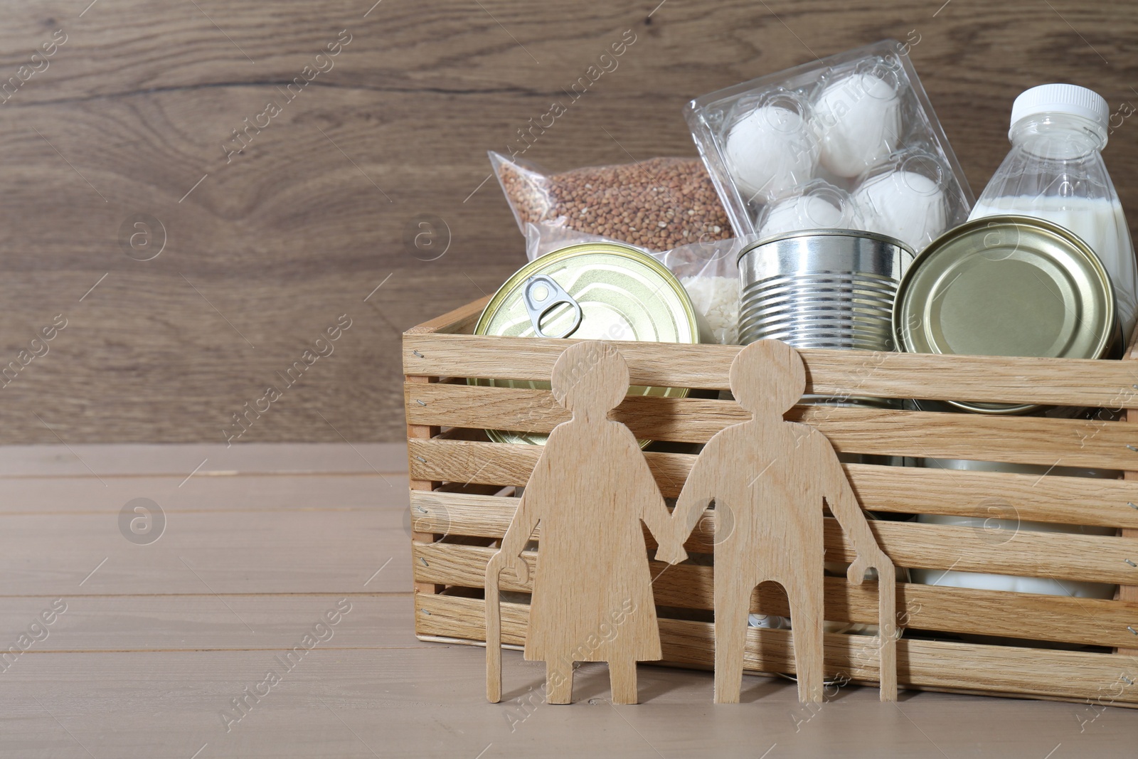 Photo of Humanitarian aid for elderly people. Donation box with food products and figure of senior couple isolated on wooden table, space for text