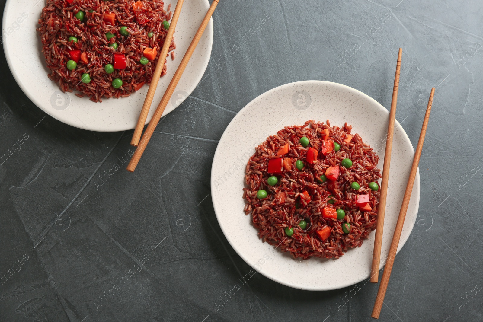 Photo of Tasty brown rice with vegetables on dark grey table, flat lay