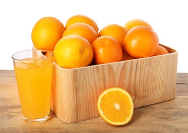 Photo of Fresh oranges in crate and glass of juice on wooden table against white background