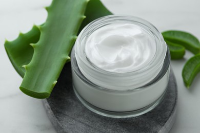 Jar with cream and cut aloe leaves on white marble table, closeup