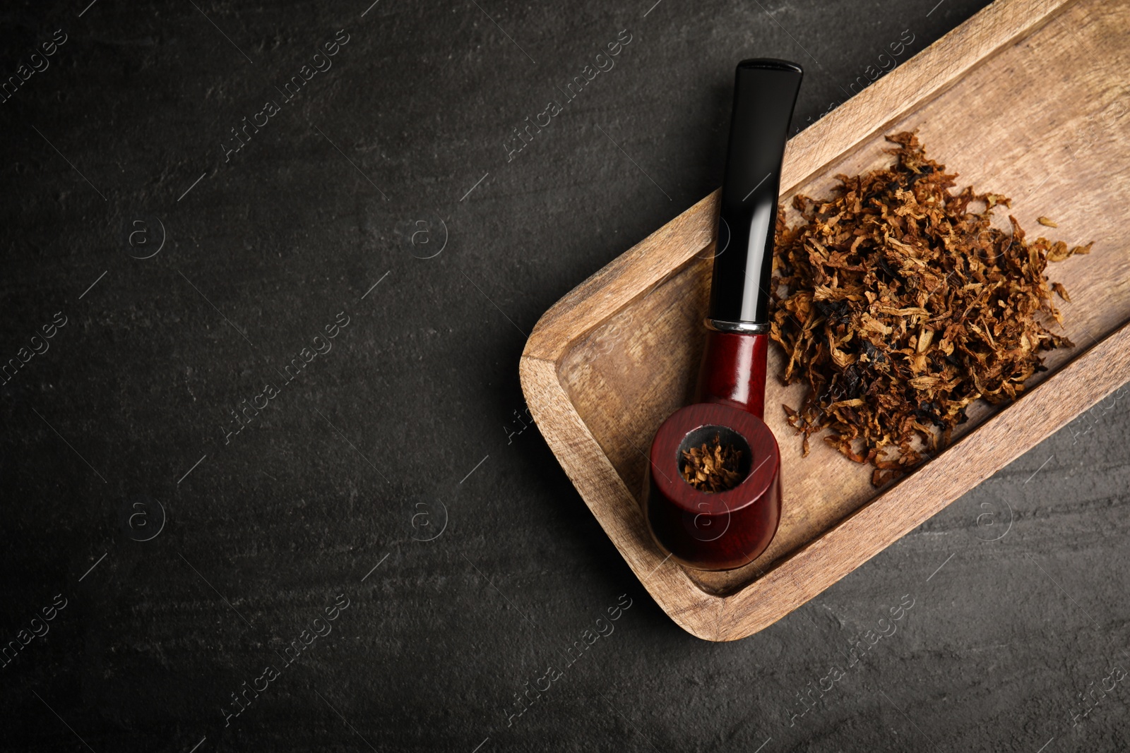 Photo of Tray with smoking pipe and dry tobacco on black table, top view. Space for text