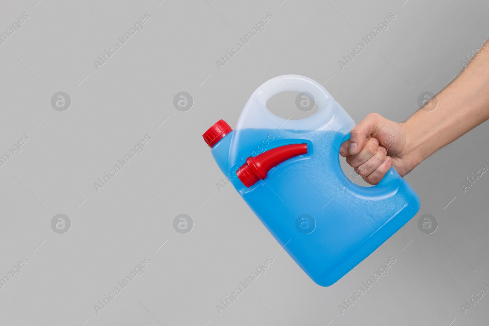 Photo of Man holding canister with blue liquid on light grey background, closeup. Space for text