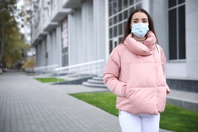 Young woman in medical face mask walking outdoors. Personal protection during COVID-19 pandemic