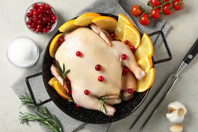 Photo of Chicken with orange slices, red berries and rosemary in round baking pan on light grey table, flat lay