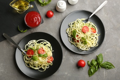Photo of Delicious zucchini pasta with cherry tomatoes and basil served on light grey table, flat lay