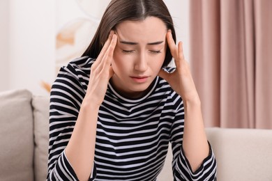 Sad woman suffering from headache on sofa indoors