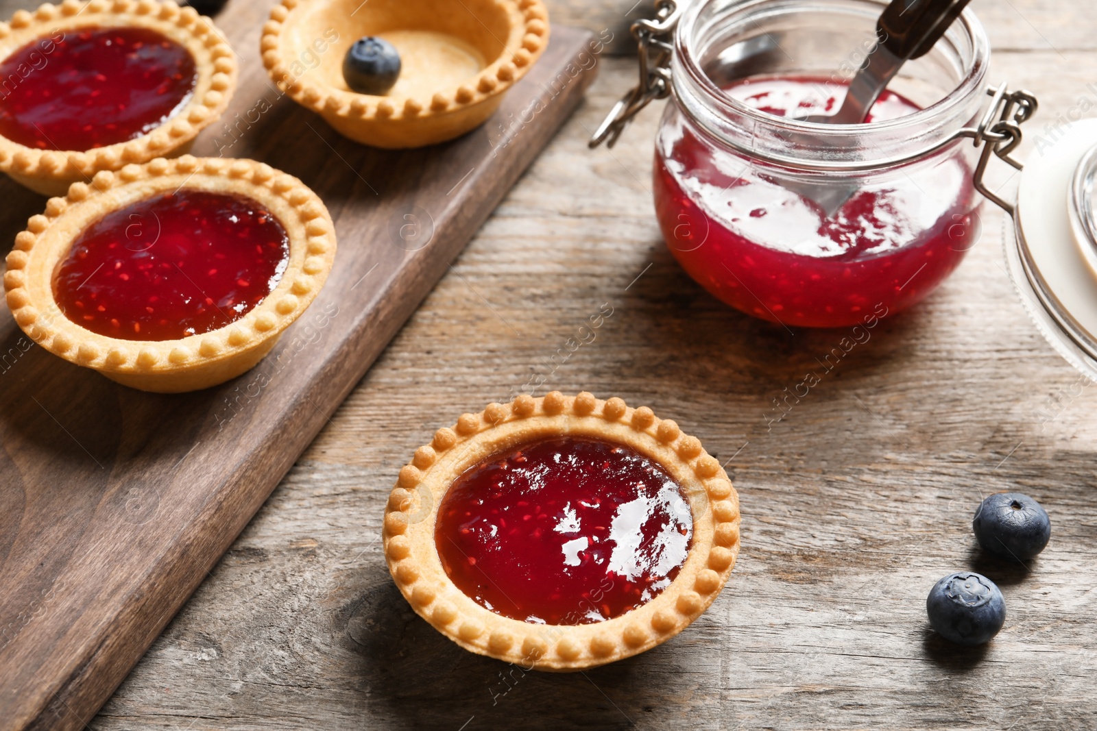 Photo of Tasty tartlets with jam on wooden background