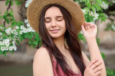 Beautiful woman in straw hat near blossoming tree on spring day