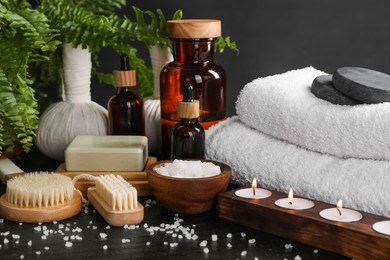 Photo of Spa composition. Brushes, soap bar, sea salt and burning candles on black table