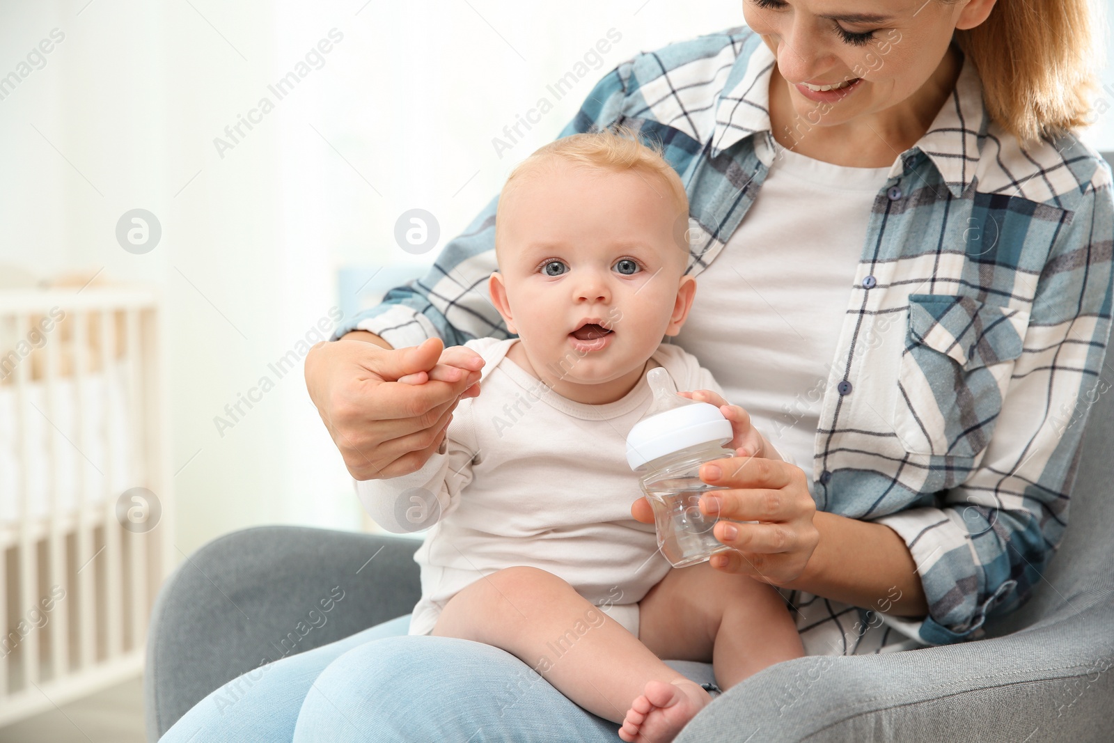 Photo of Lovely mother giving her baby drink from bottle in room