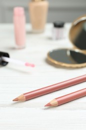 Lip pencils and other makeup products on white wooden table