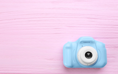 Light blue toy camera on pink wooden background, top view. Space for text