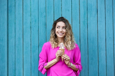 Happy young woman with delicious ice cream in waffle cone near wooden wall
