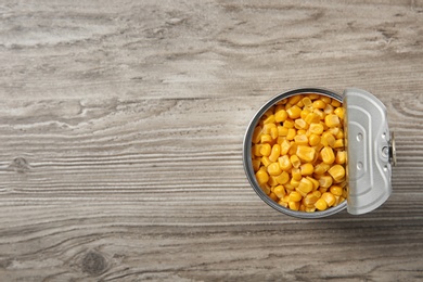 Open tin can of corn kernels on wooden background, top view. Space for text