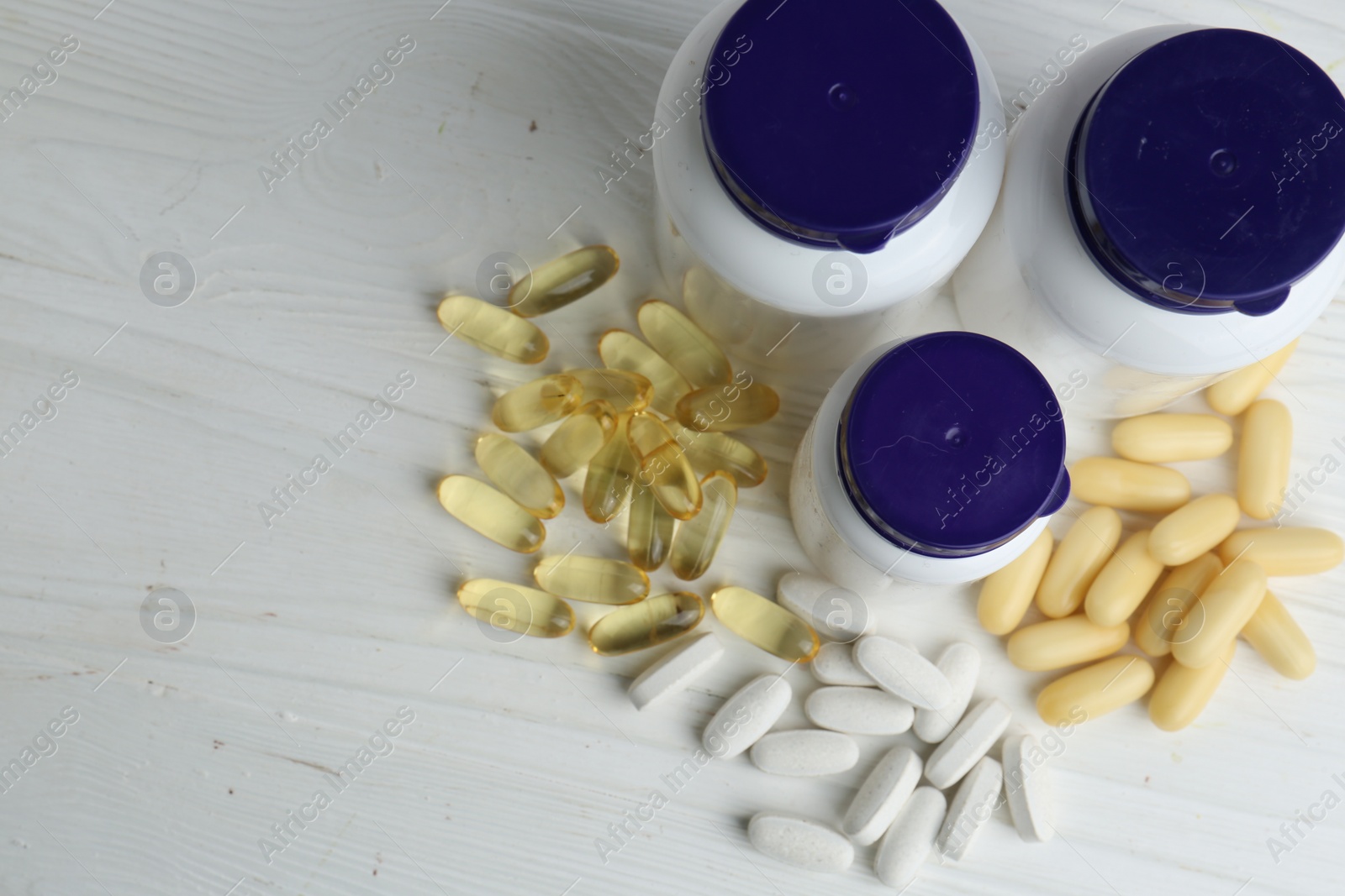 Photo of Medical bottles and pills on white wooden table, above view. Space for text