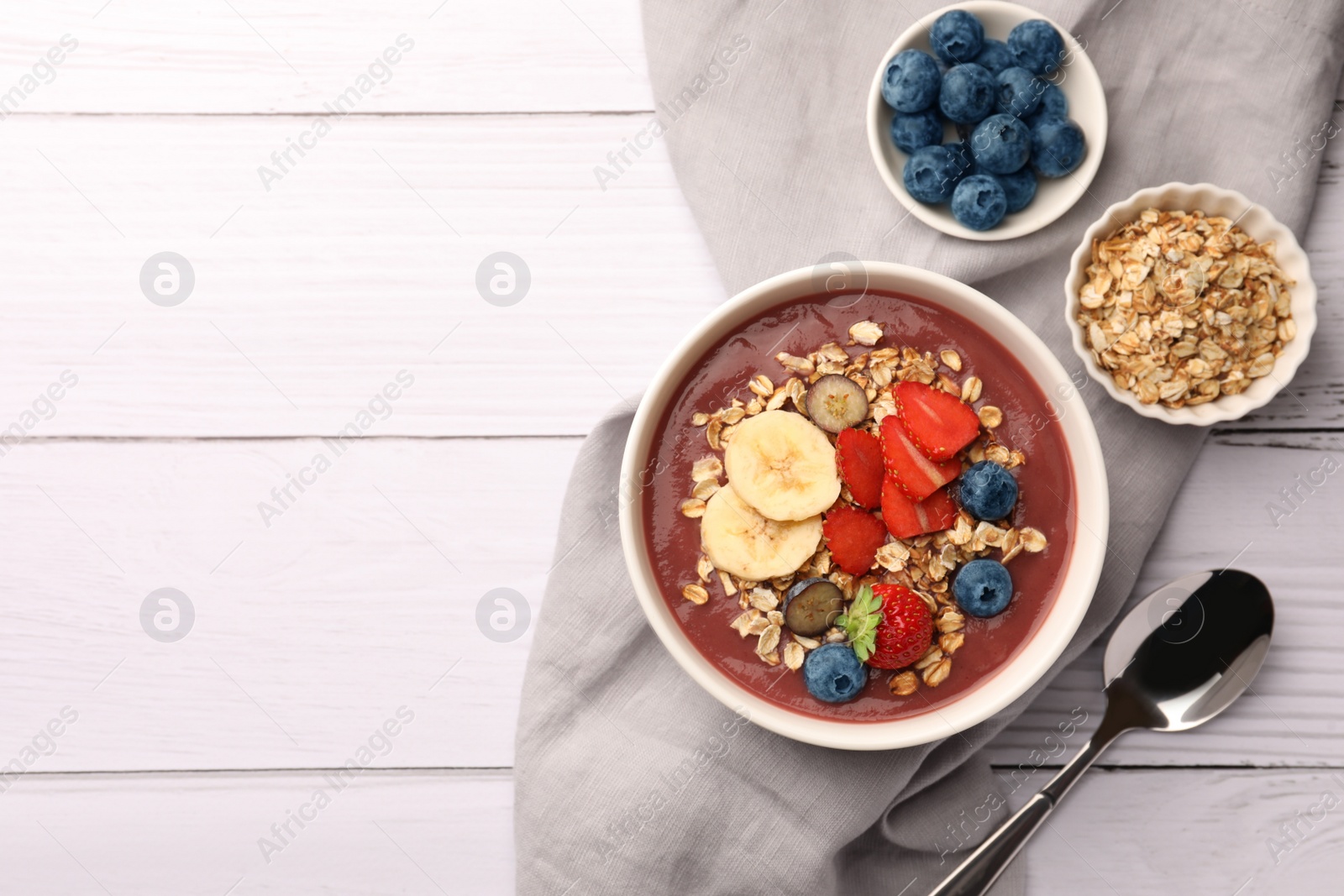 Photo of Delicious smoothie bowl with fresh berries, banana and granola on white wooden table, flat lay. Space for text