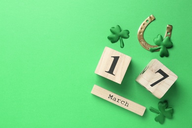 Decorative clover leaves, horseshoe and block calendar on green background, flat lay with space for text. St. Patrick's Day celebration