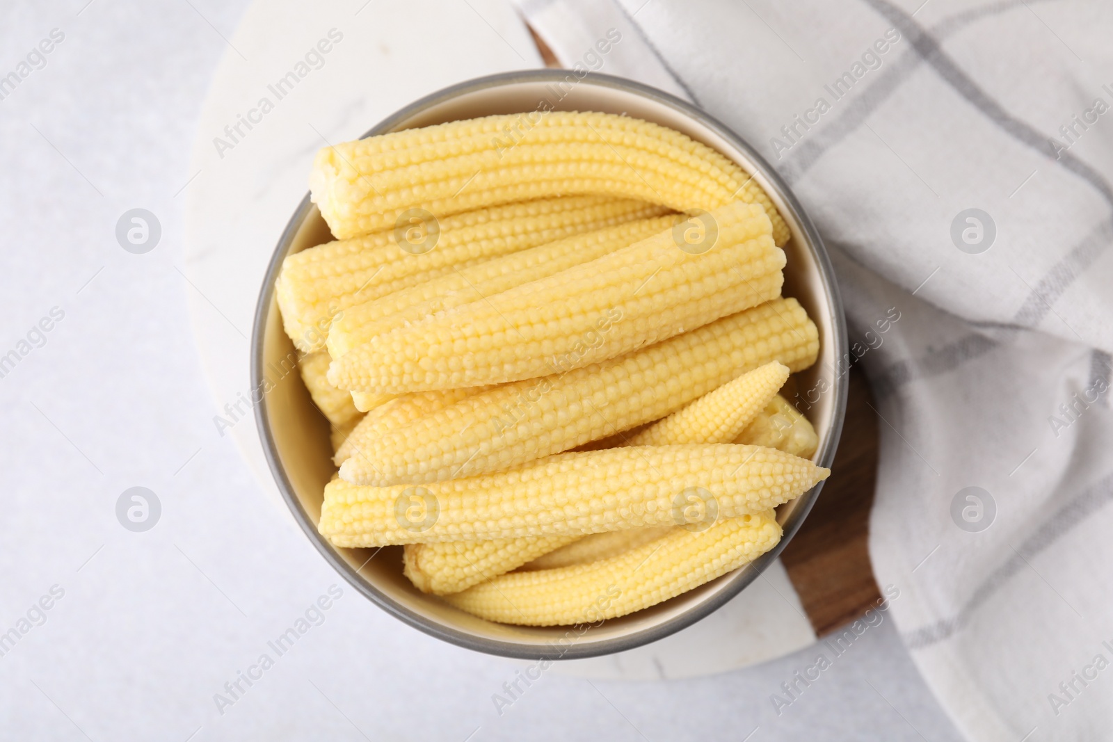 Photo of Tasty fresh yellow baby corns in bowl on white table, top view