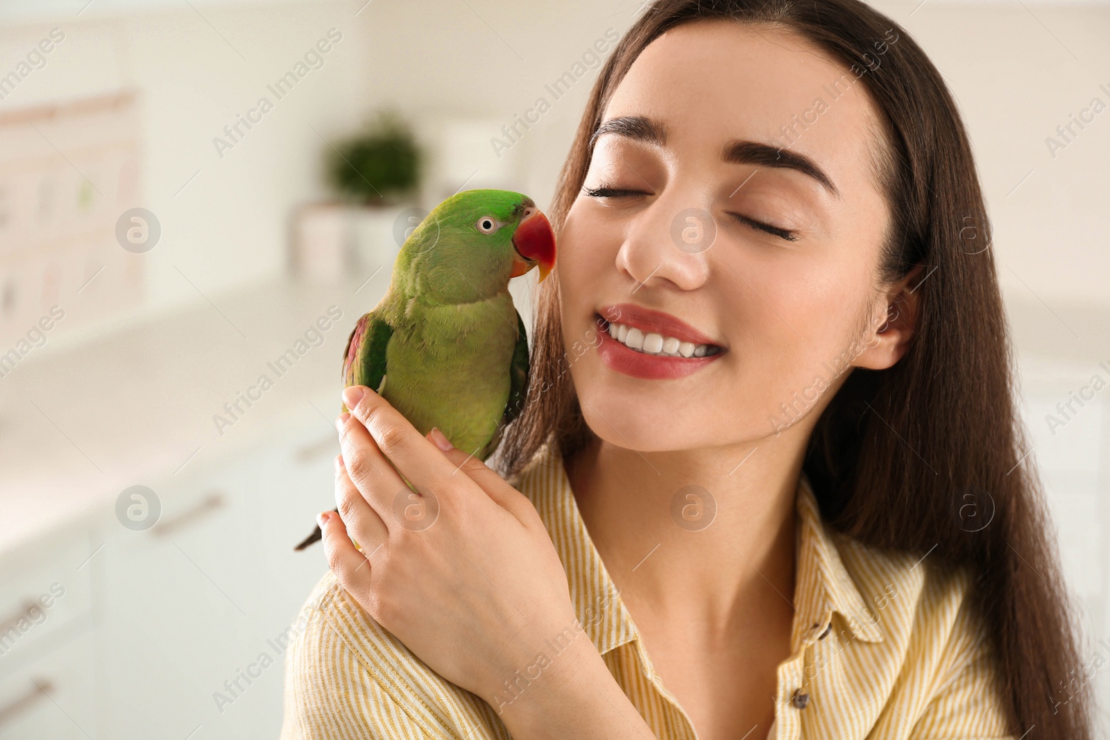 Photo of Young woman with Alexandrine parakeet indoors. Cute pet