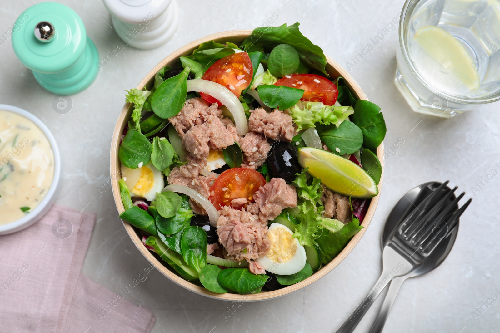 Photo of Bowl of delicious salad with canned tuna and vegetables served on light table, flat lay