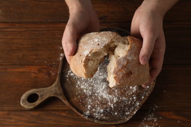 Photo of Man breaking loaf of fresh bread at wooden table, top view