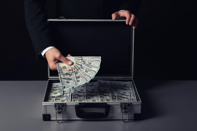 Photo of Businessman with suitcase full of money on dark background
