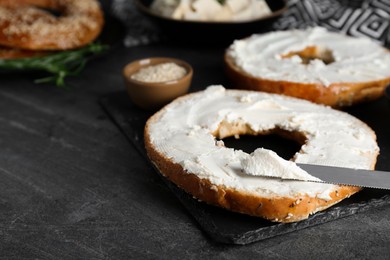 Photo of Delicious bagel with tofu cream cheese and knife on black table, closeup. Space for text