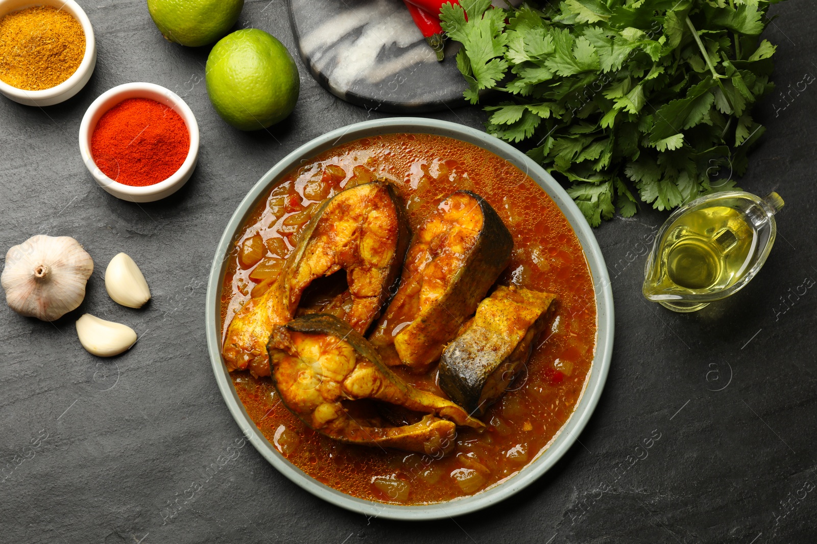 Photo of Tasty fish curry and ingredients on grey textured table, flat lay. Indian cuisine