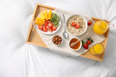 Photo of Tasty breakfast served in bed. Oatmeal, juice, fruits, almonds and honey on tray, top view
