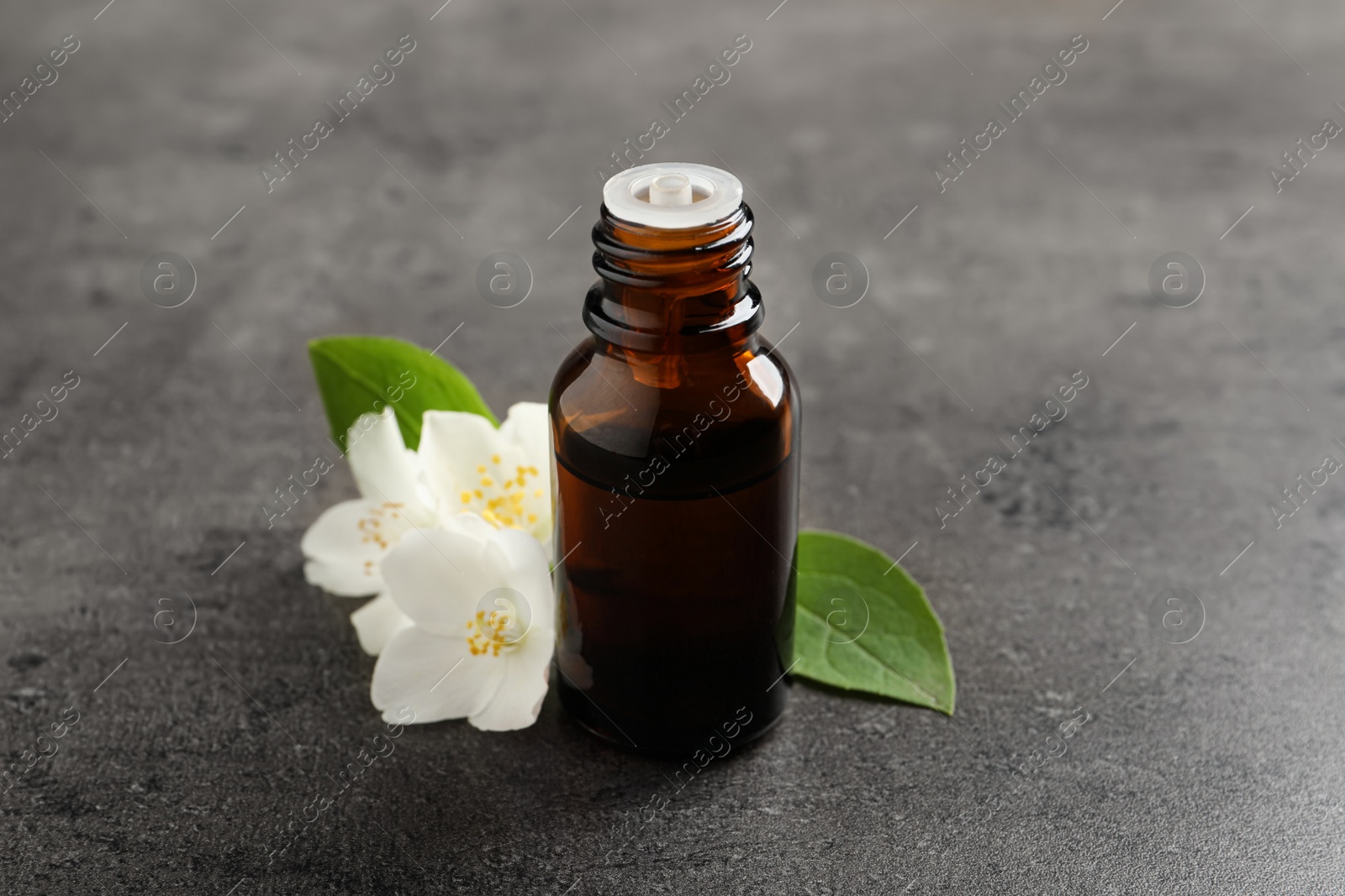 Photo of Essential oil and jasmine flowers on grey table, closeup