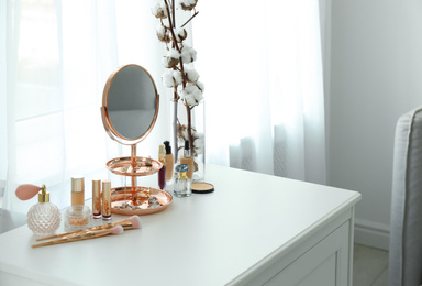 Photo of Small mirror and different makeup products on chest of drawers indoors. Space for text