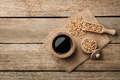 Photo of Soy sauce in bowl and soybeans on wooden table, flat lay. Space for text