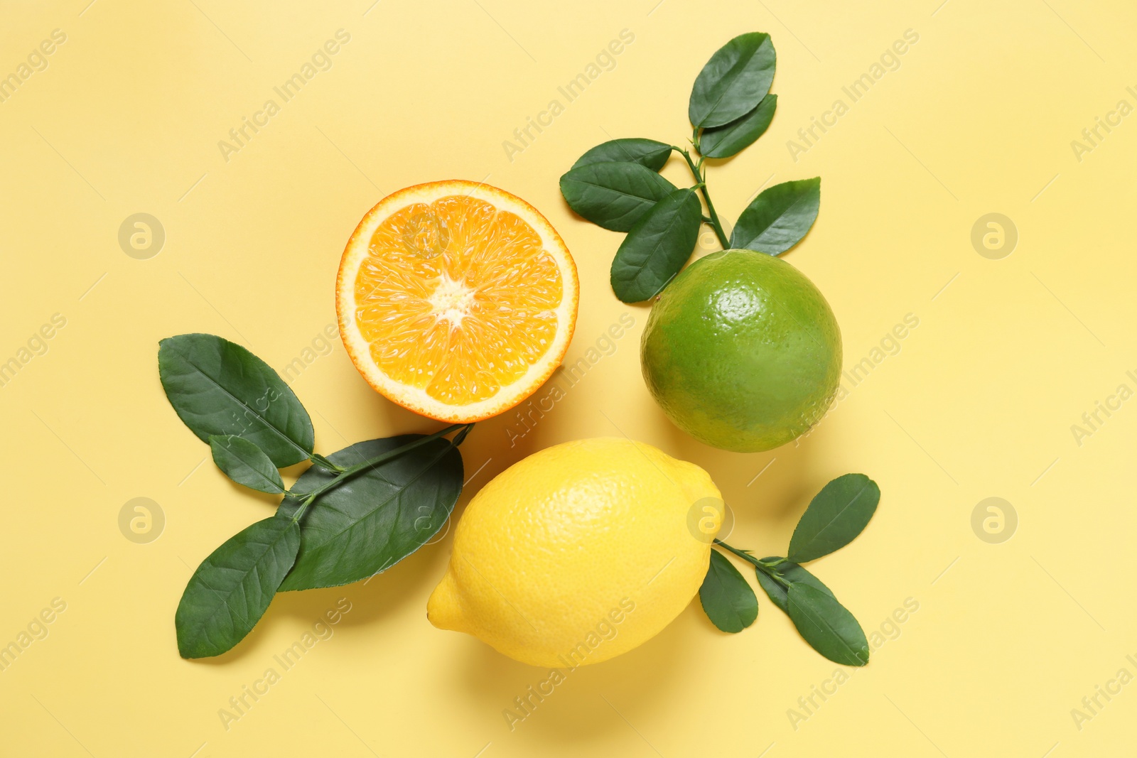 Photo of Different cut and whole citrus fruits on yellow table, flat lay