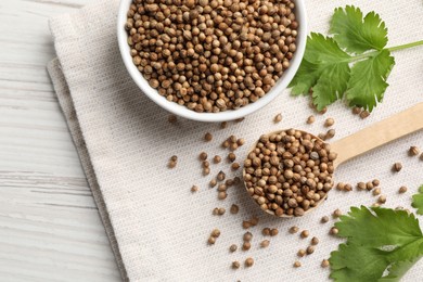 Photo of Dried coriander seeds in bowl, spoon and green leaves on wooden table, flat lay