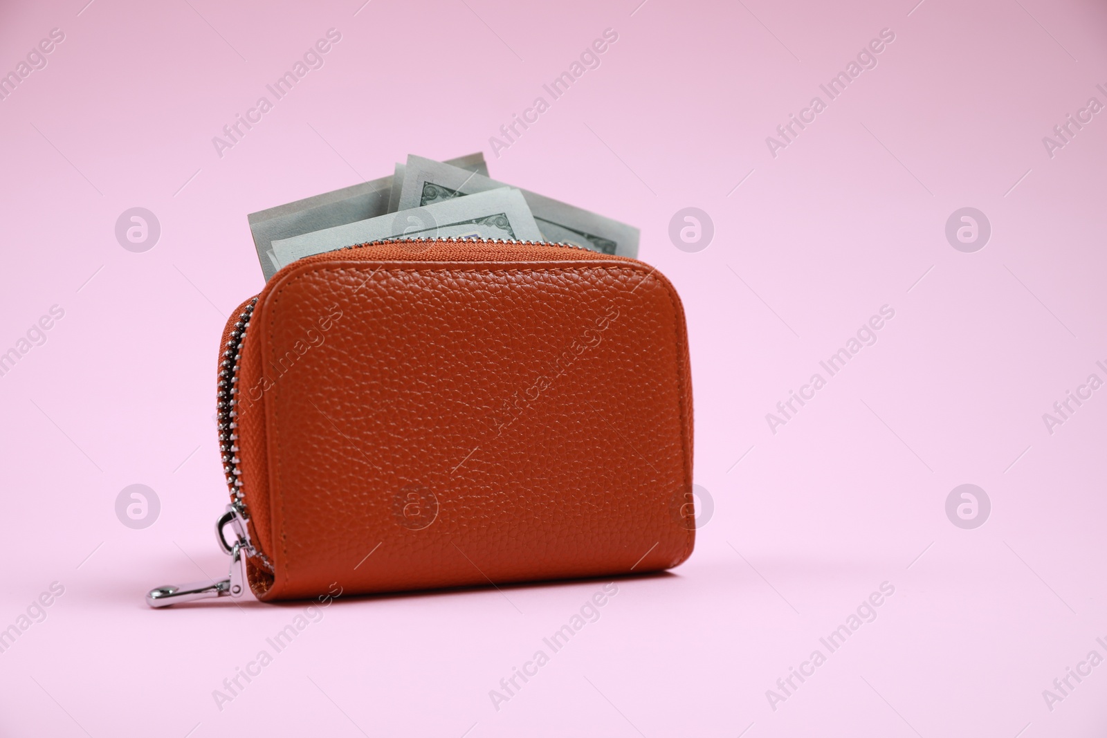Photo of Stylish brown leather purse with dollar banknotes on pink background, space for text