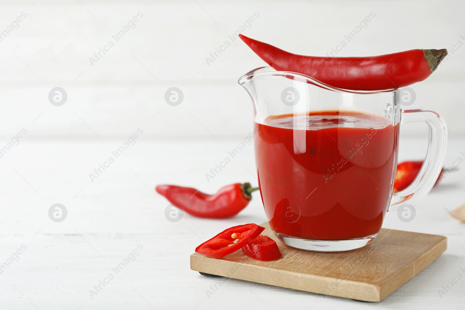 Photo of Jug with spicy chili sauce and fresh pepper on light table